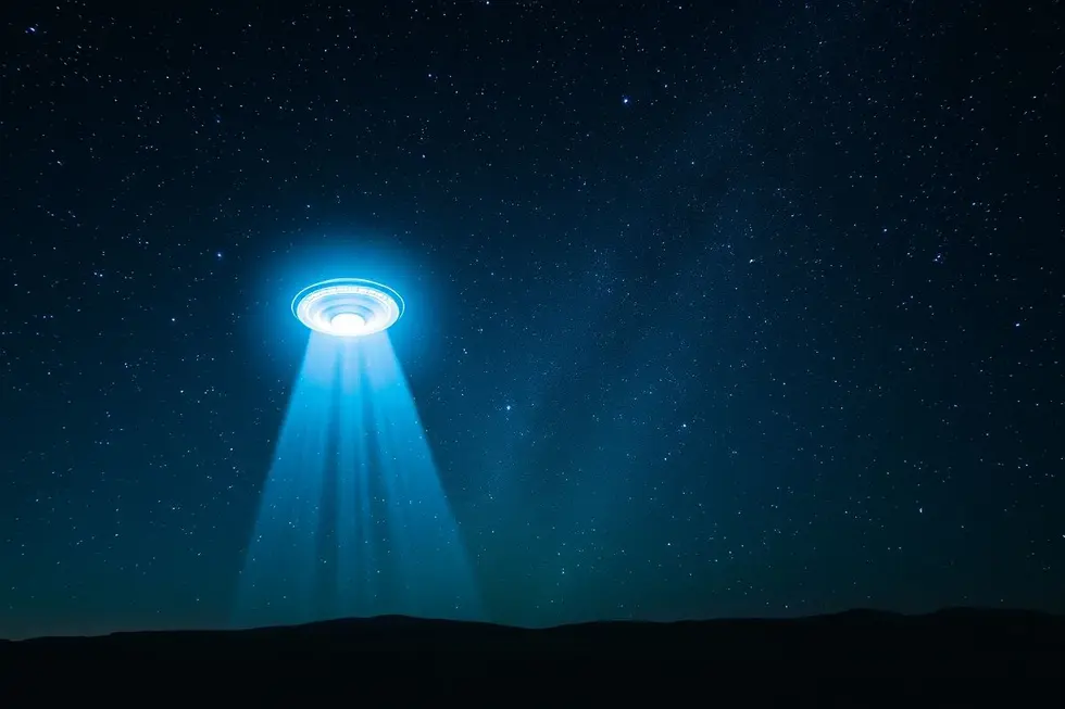 Céu noturno com um OVNI pairando sobre uma paisagem, representando a busca pela verdade sobre vida extraterrestre.