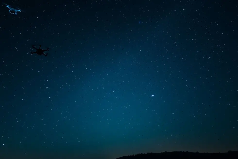 Céu estrelado com drones e silhueta de um OVNI.